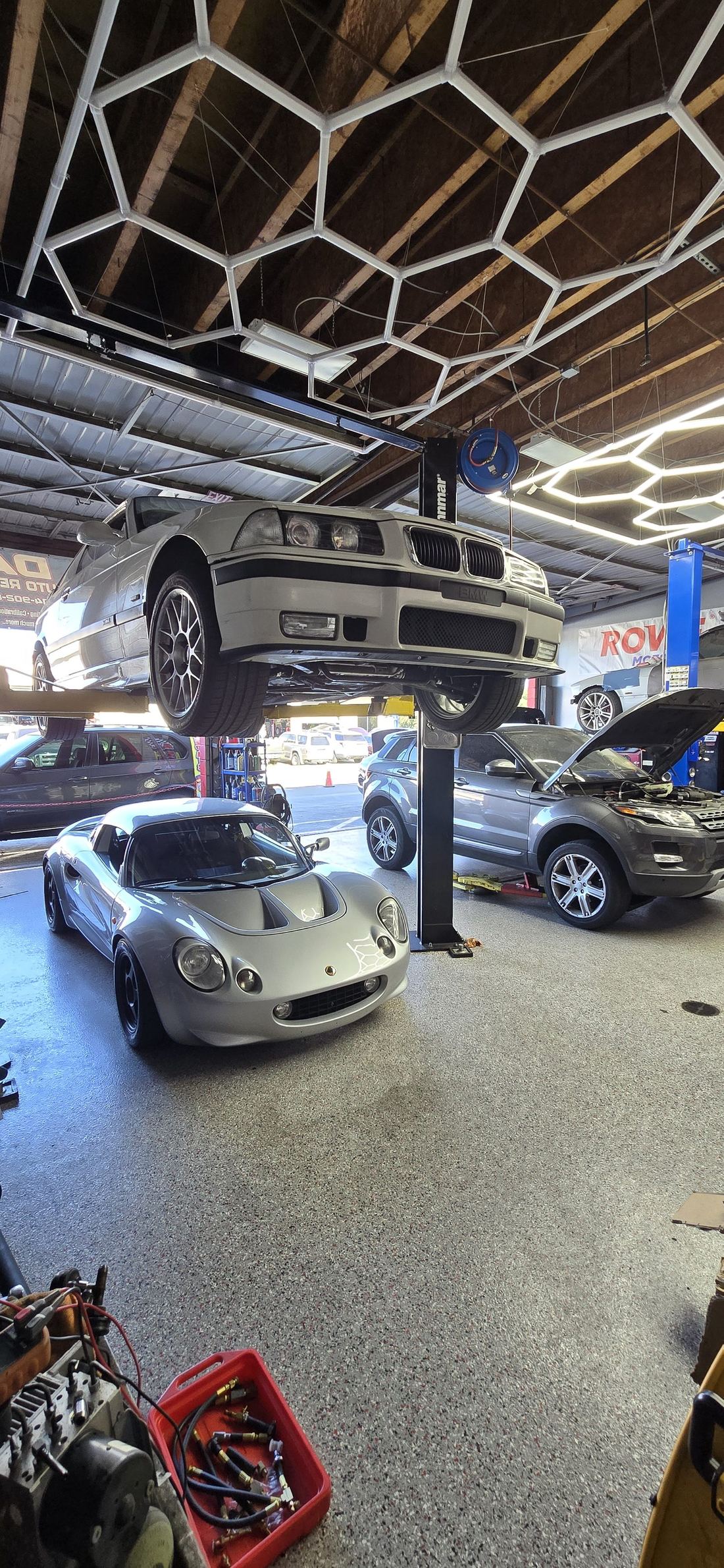 BMW on the lift alongside a Lotus and Range Rover in the shop